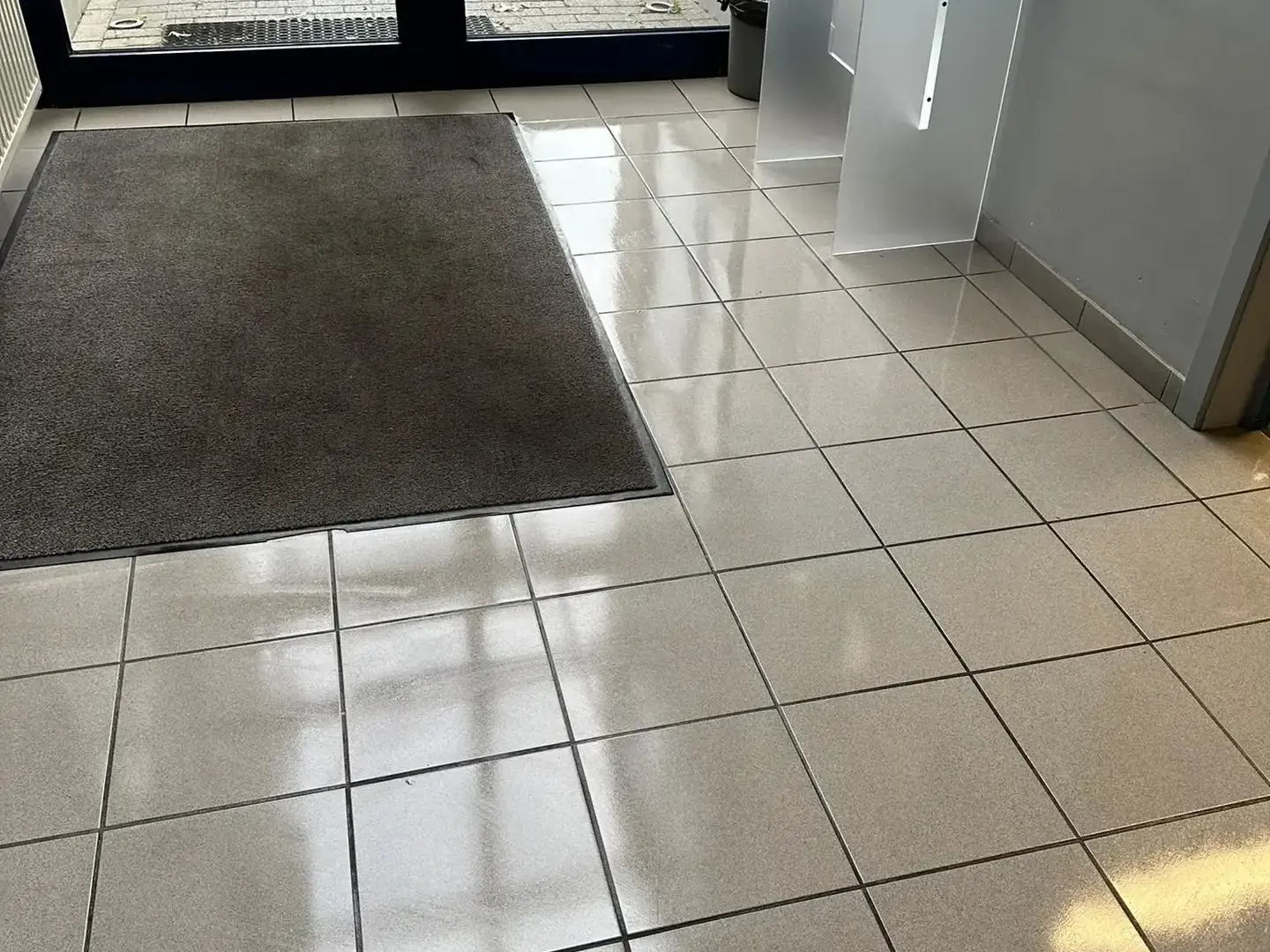 Le même hall d'entrée après intervention : carrelage brillant et paillasson remis en place.